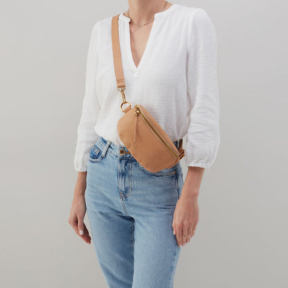 person wearing white shirt, blue jeans, and sandstorm fern bag as a crossbody.