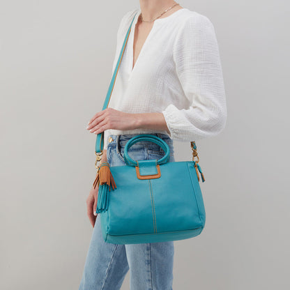 woman wearing jeans and a white blouse with an aqua sheila medium bag over her shoulder.