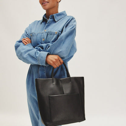 person wearing denim outfit and holding black tote.