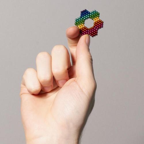 hand holding a flower shape made from rainbow colored magnetic balls.