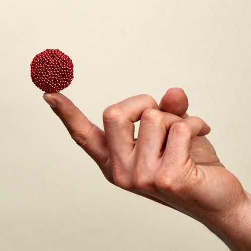 hand with finger extended with a ball made from red magnetic balls on the tip o f finger on cream background.