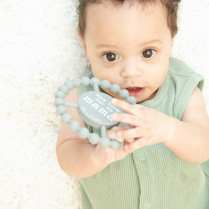 a baby boy laying on a plush blanket while holding the mad love for mama teether 