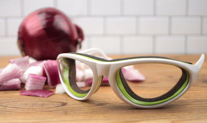 onion goggles on wood countertop with whole and chopped onions.