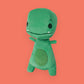 tiny t rex plush toy on a coral background