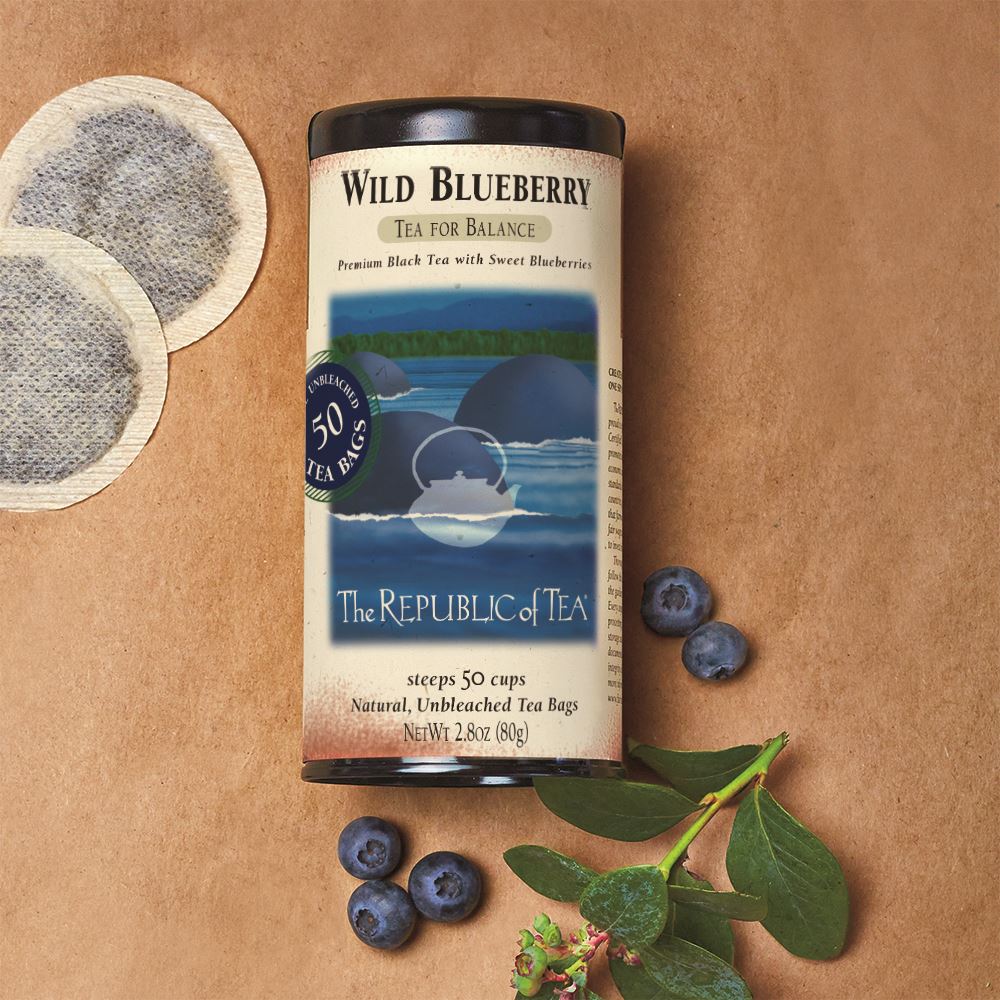 wild blueberry black tea canister displayed next to two tea bags, blueberries, and blueberry sprig on butcher paper