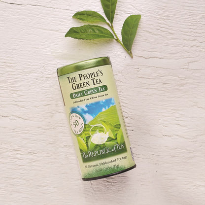 the people's green tea canister displayed next to sprig of tea leaves on a white wooden surface