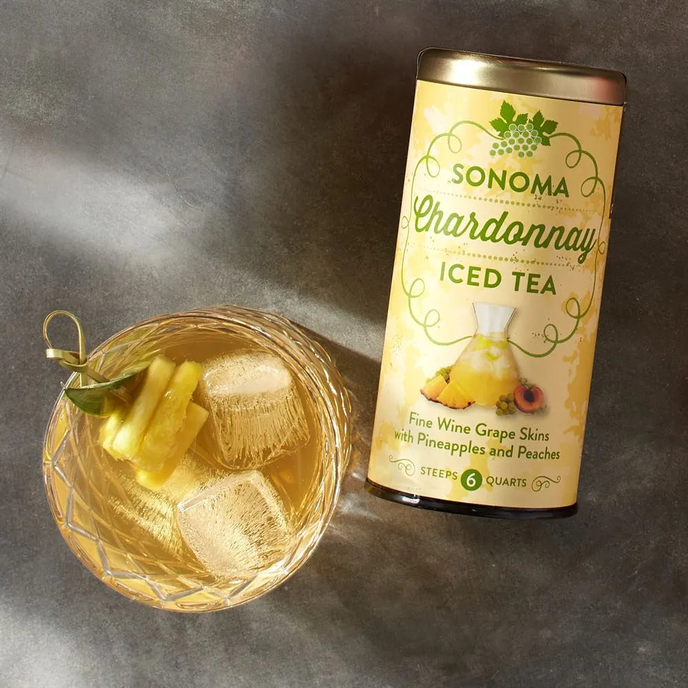 sonoma chardonnay iced tea canister laying on a gray surface next to a glass of tea with pinapple slices