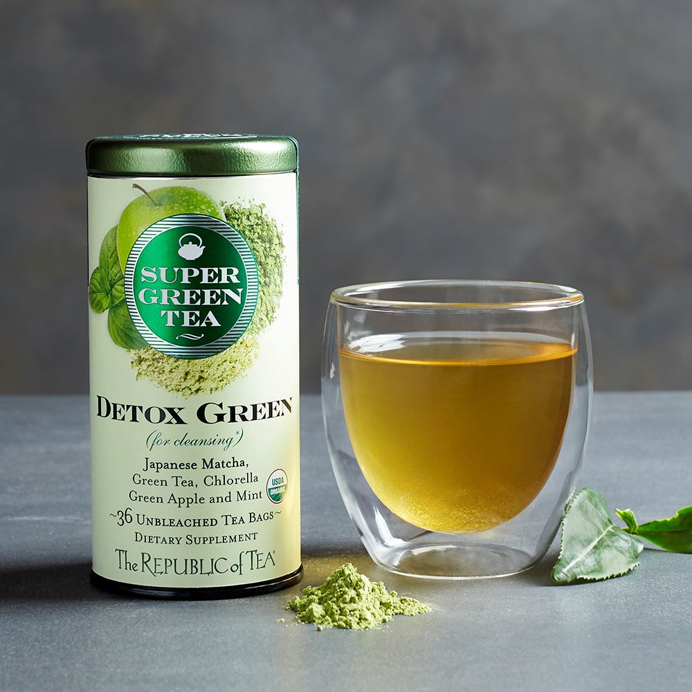 detox green tea canister displayed next to a glass cup of tea and tea leaves on a gray surface
