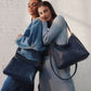 two women and one wearing the denim cambel crossbody against a white brick wall