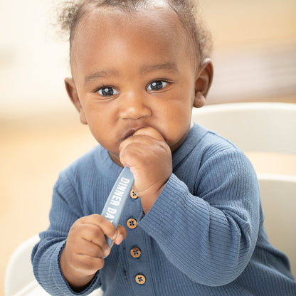 a baby boy sitting in a highchair chewing on the blue spoon
