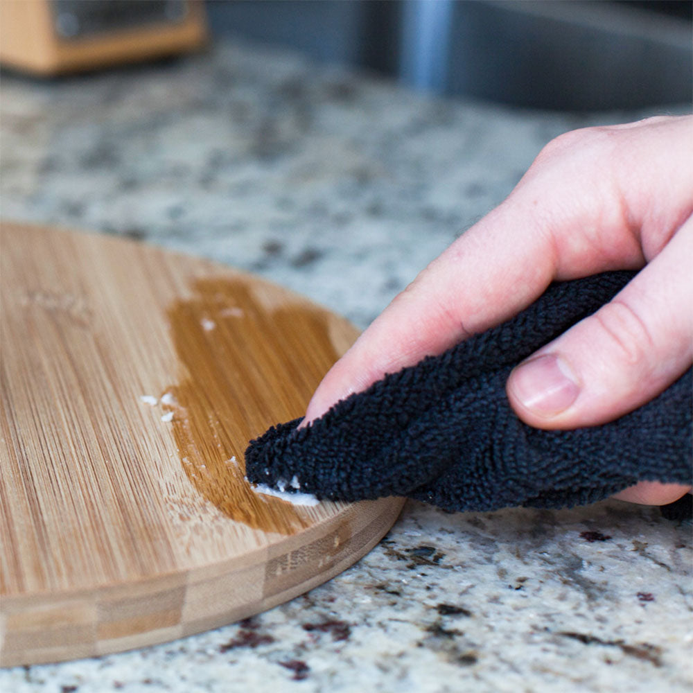 the natural wood wax being used on a wood cutting board on a marble countertop 