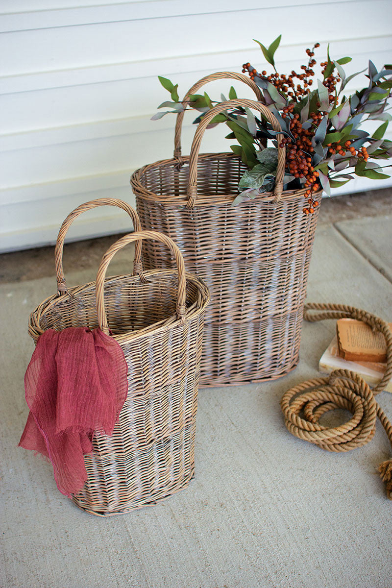 small and large tall oval wicker baskets displayed with a sheer scarf greenery bunch next to a knotted rope against a white slatted wall