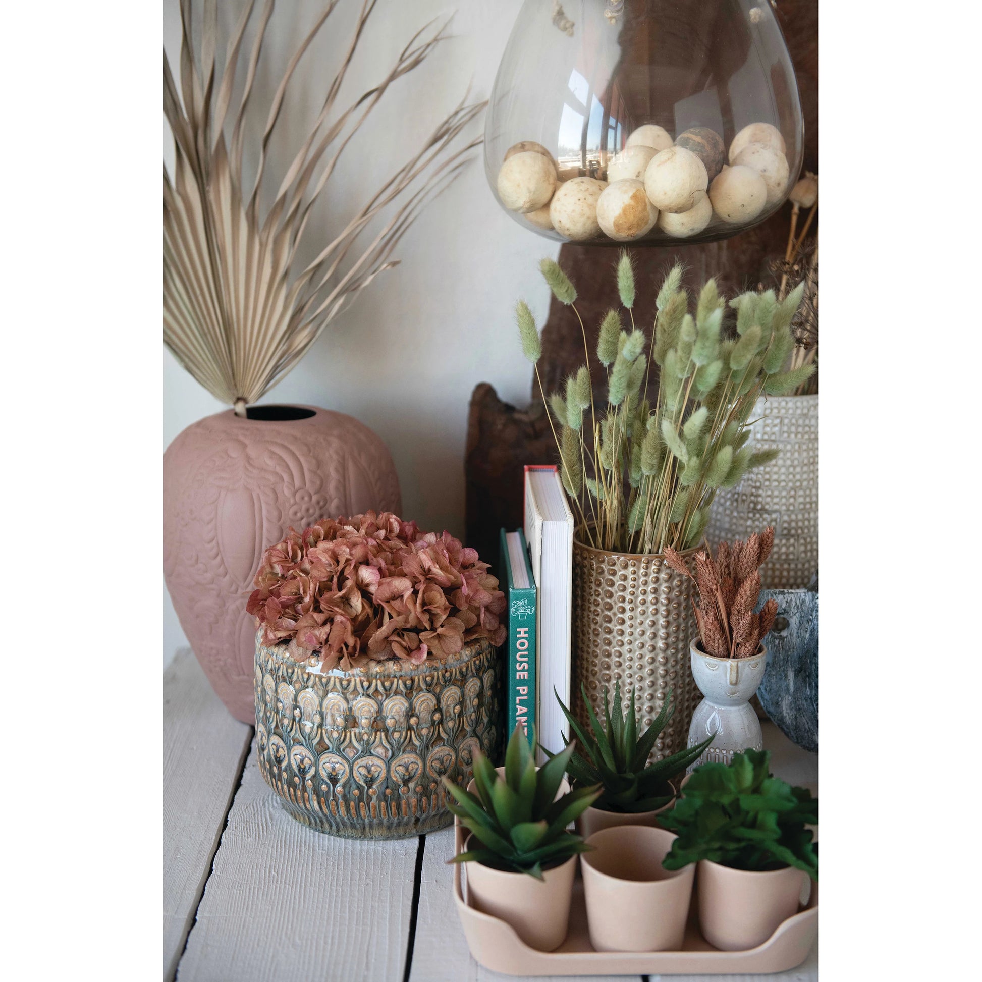 embossed planter displayed with greenery vases succulents and books on a white background