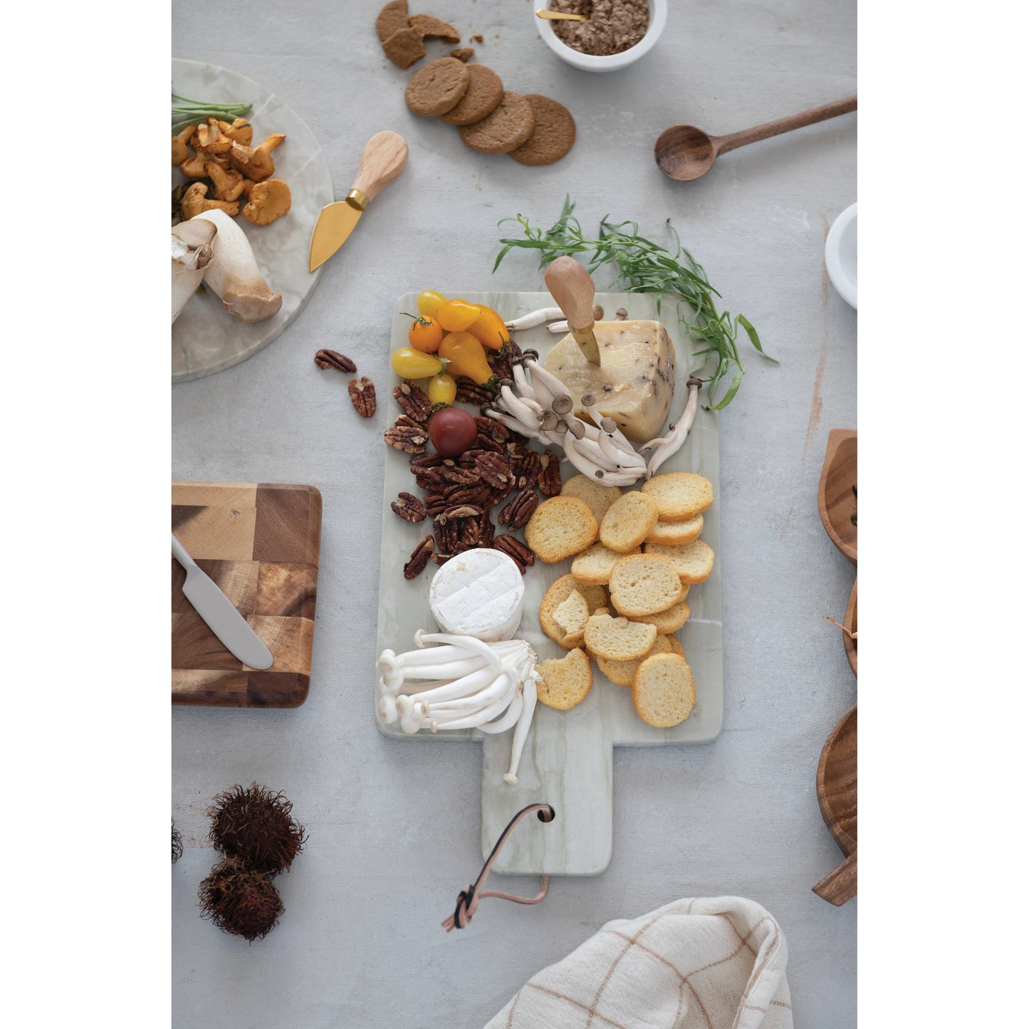 marble cheese cutting board with leather strap displayed with charcuterie foods and serving trays on a white background