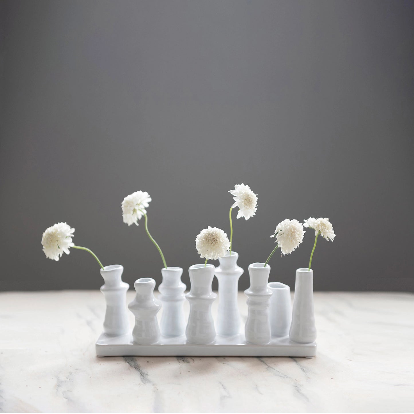 stoneware multi vase displayed with white flowers in a few displayed on a distressed white table against a gray background