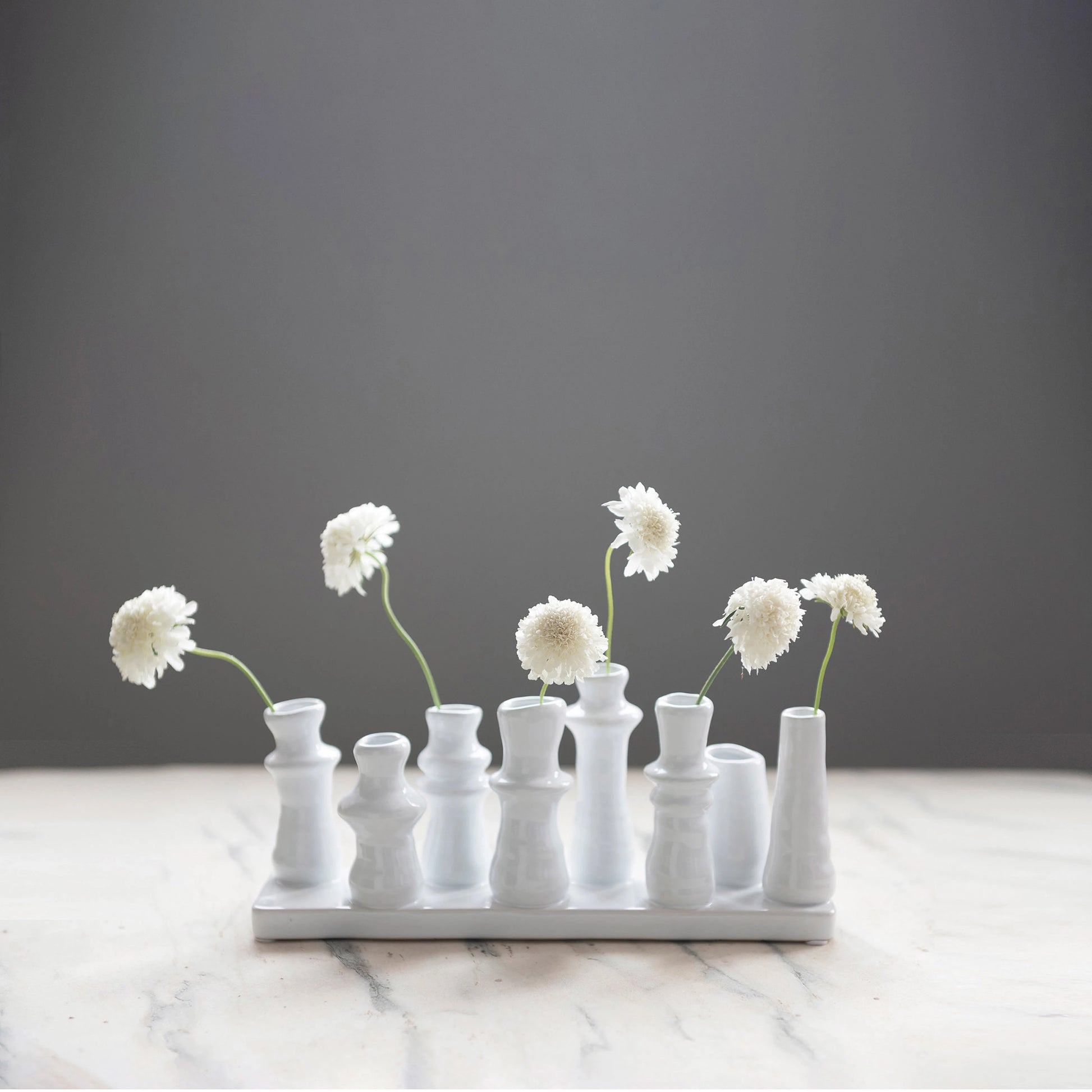 stoneware multi vase displayed with white flowers in a few displayed on a distressed white table against a gray background
