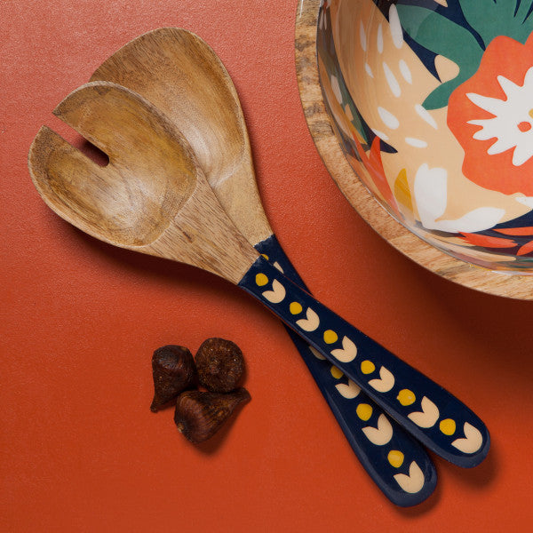 wooden salad servers with blue handles with floral design nest to salad bowl and figs.