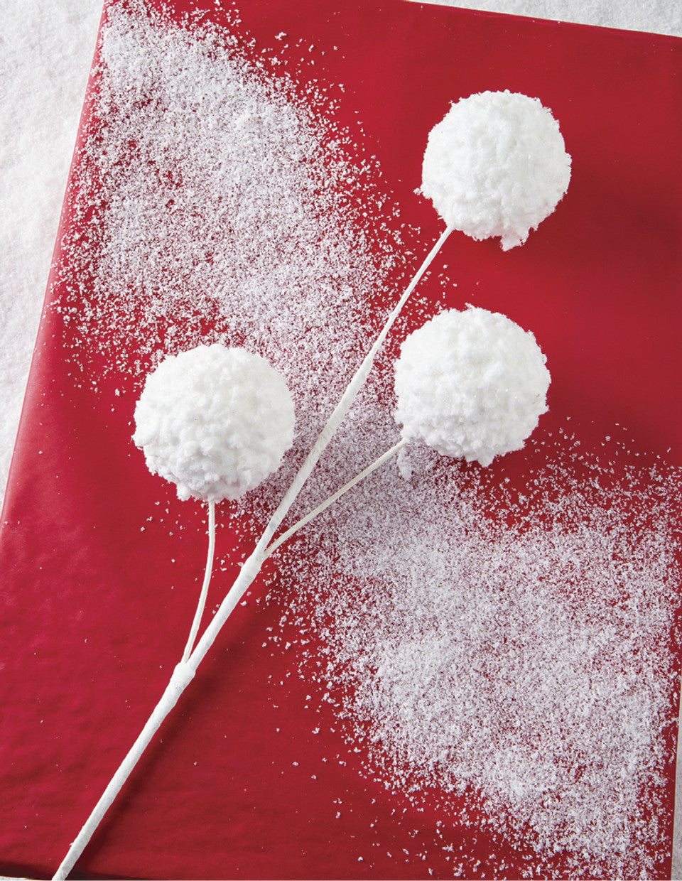 white wired stem with 3 snowballs on the end of each wire laying on a red background with a dusting of snow.