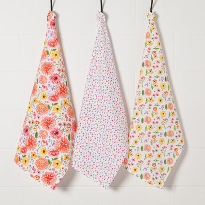 3 white dishtowels with floral designs hanging on hooks.