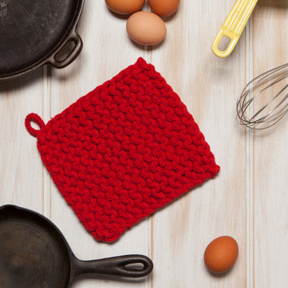 red knit pot holder on a table with pots and pans around it and eggs and utensils near by.