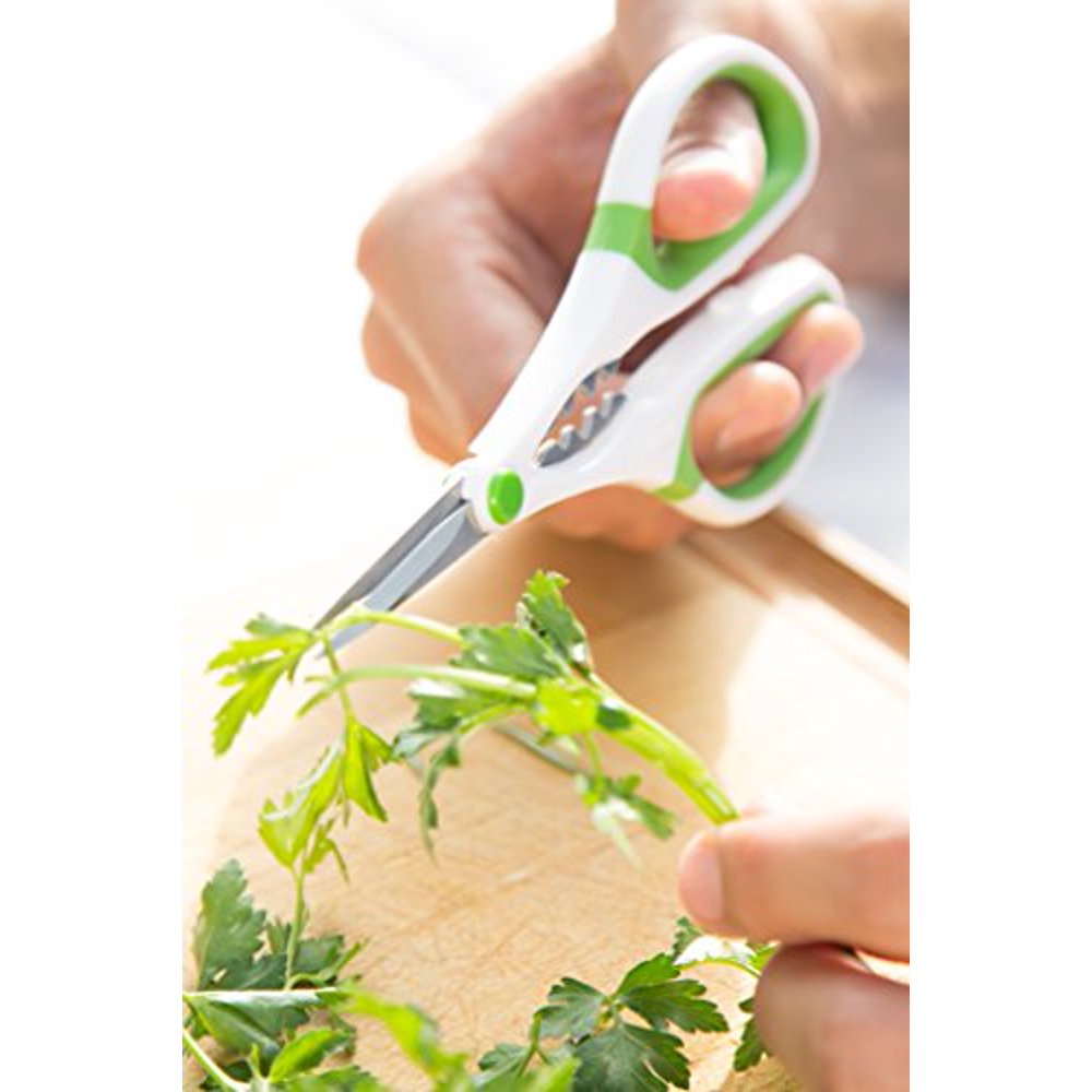 hands snipping herbs over a wooden cutting board