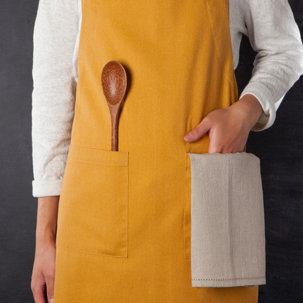 person wearing apron with wooden utensil and towel in apron pocket.
