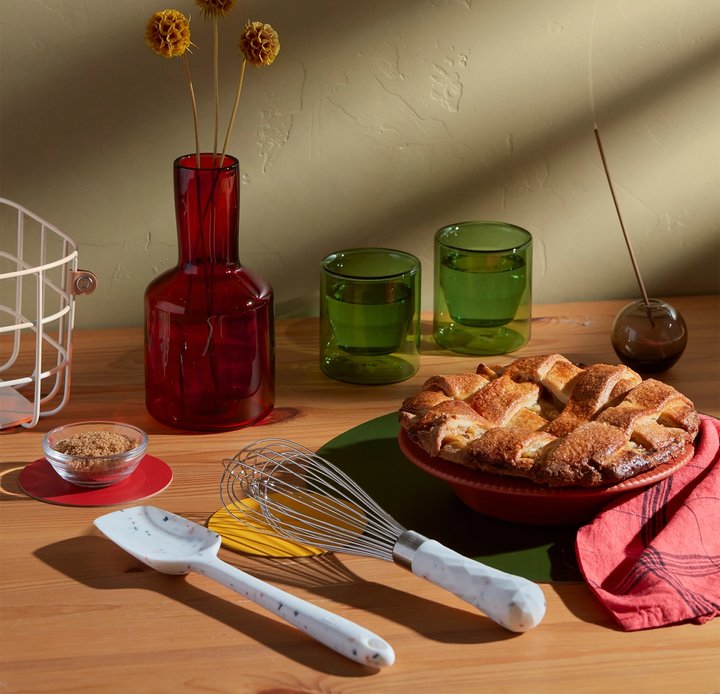 the barcelona ultimate whisk displayed beside a pie dish and spices with a vase and glasses on a wood table