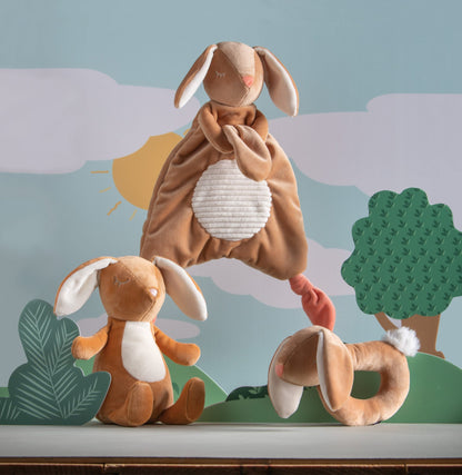 leika little bunny lovey displayed next to the bunny and bunny rattle against a depiction of the outdoors 