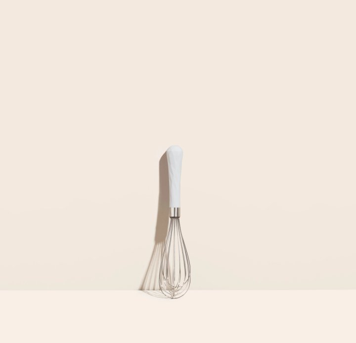 mini whisk leaning against a cream colored background.