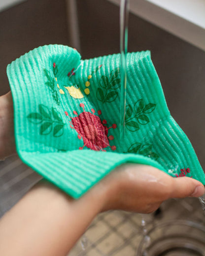 hands holding swedish dish cloth under sink faucet.