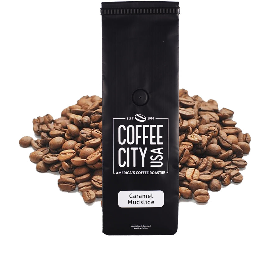 a black coffee bag filled with caramel mudslide coffee with a pile of coffee beans behind it on a white background