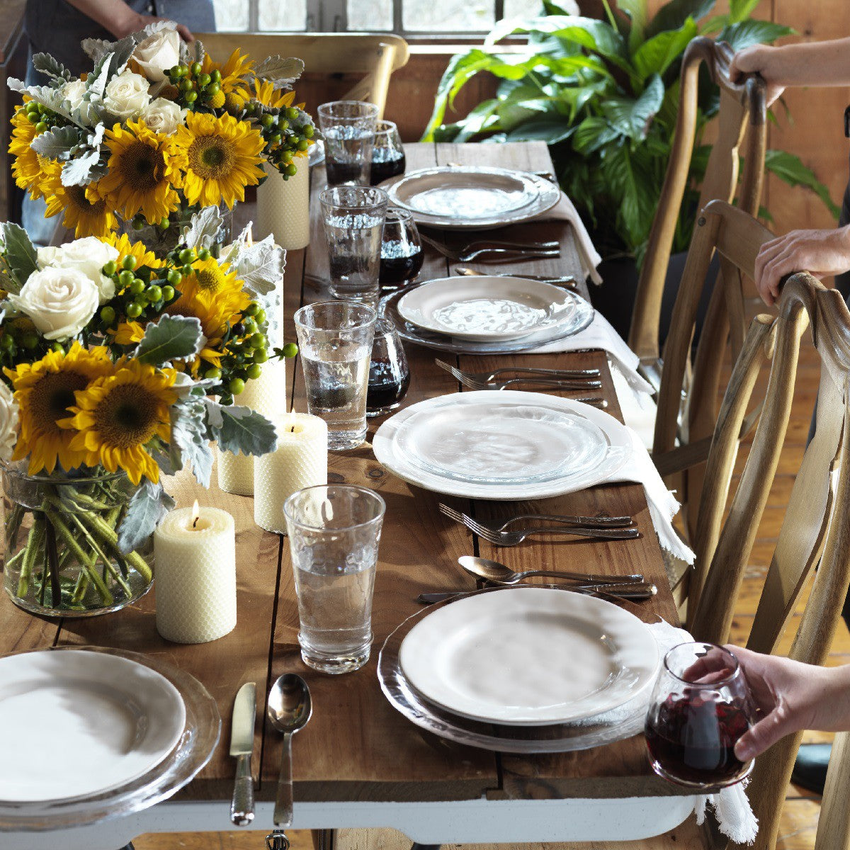 table setting on a rustic wooden table with glasses, flatware, candles and sunflowers.