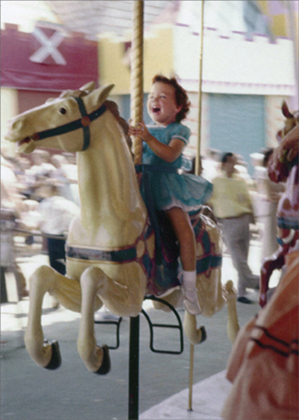front of card is a photograph of a joyful child riding a carousel 