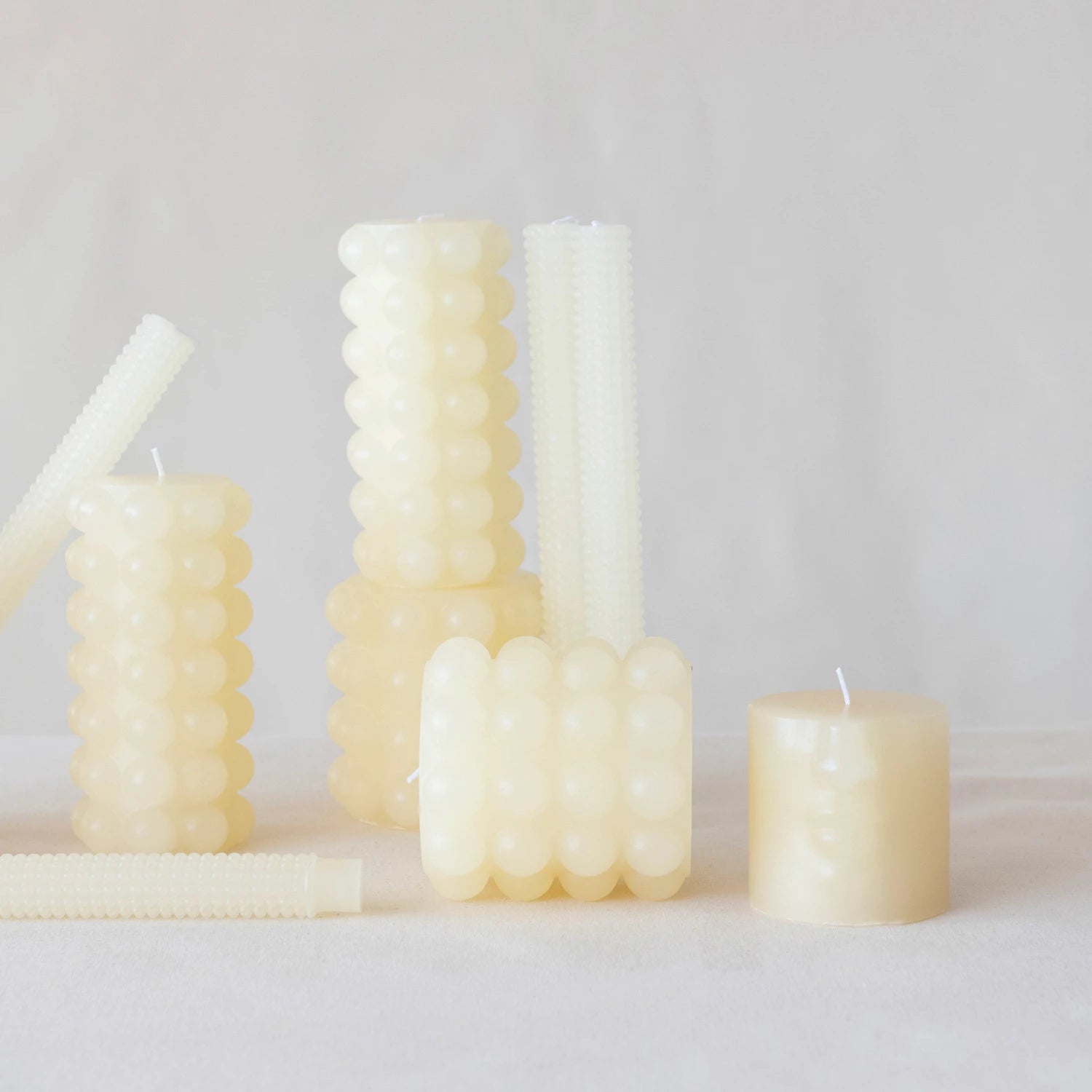 multiple sizes of cream hobnail pillar candles displayed together on against a gray background