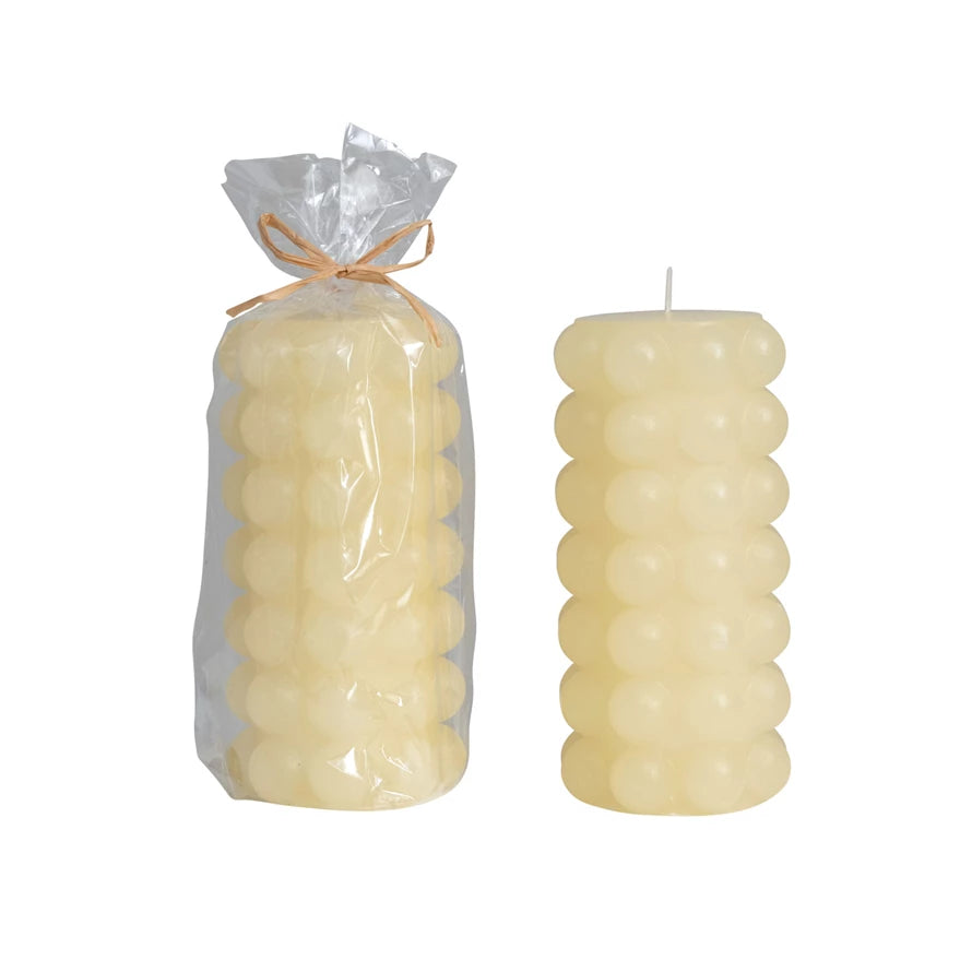 one tall cream hobnail pillar candle in clear wrap tied with twine and one with out packaging on a white background