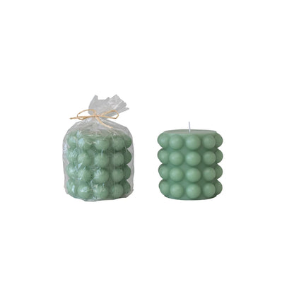 one small teal hobnail pillar candle in clear wrap with twine bow and one without the package on a white background