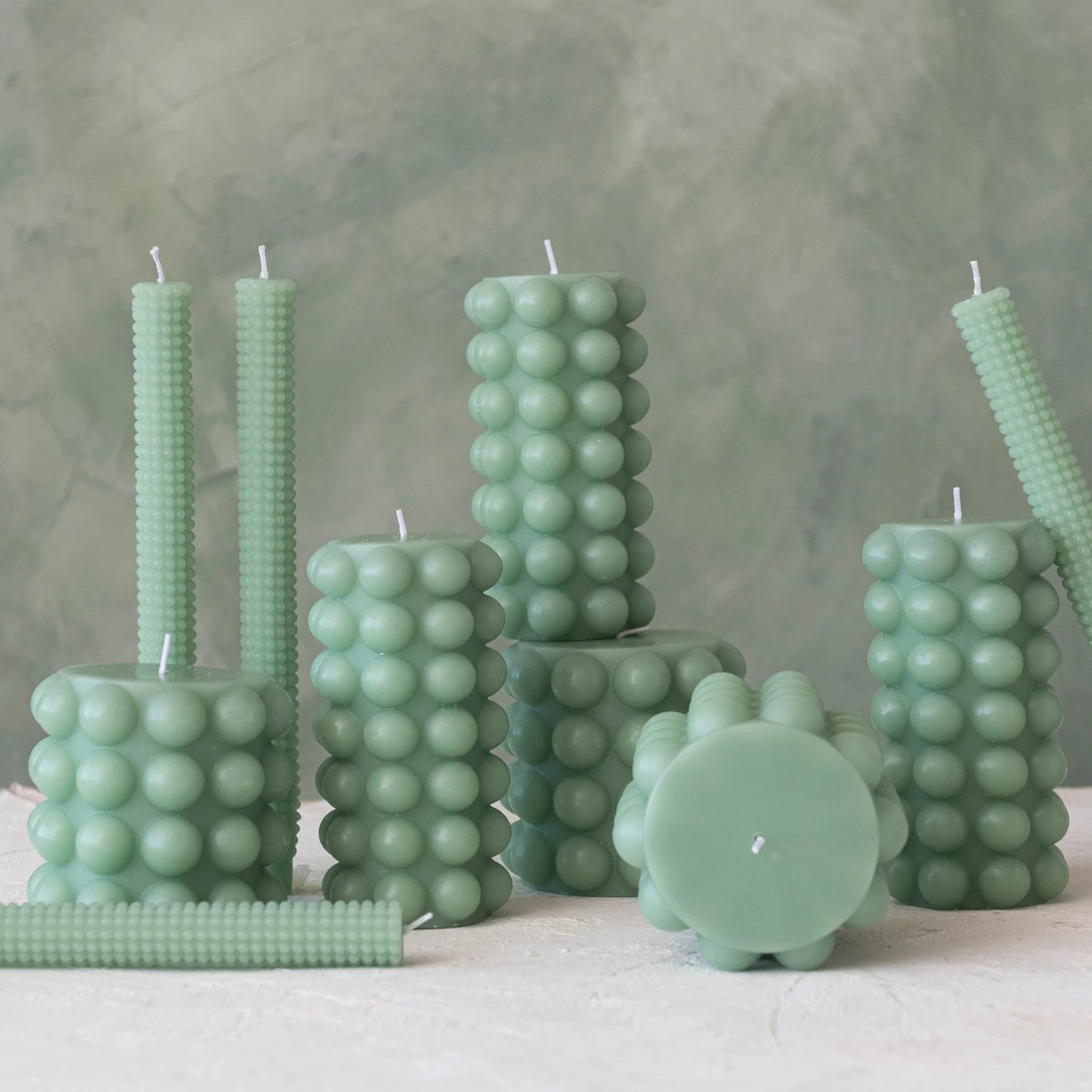 multiple sizes of teal hobnail pillar candles displayed together on against a gray background
