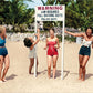 front of card has four women standing on a beach with a sign