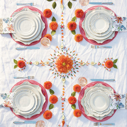 table setting of puro dishes with pink chargers, orange flowers, floral napkins on a white tablecloth.