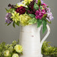 glazed ceramic pitcher filled with colorful flowers and a flower bunch next to it on a gray background