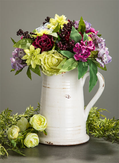 glazed ceramic pitcher filled with colorful flowers and a flower bunch next to it on a gray background