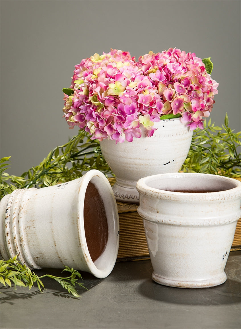all three pots displayed with pink hydrangeas on a book and laying beside it on a gray background