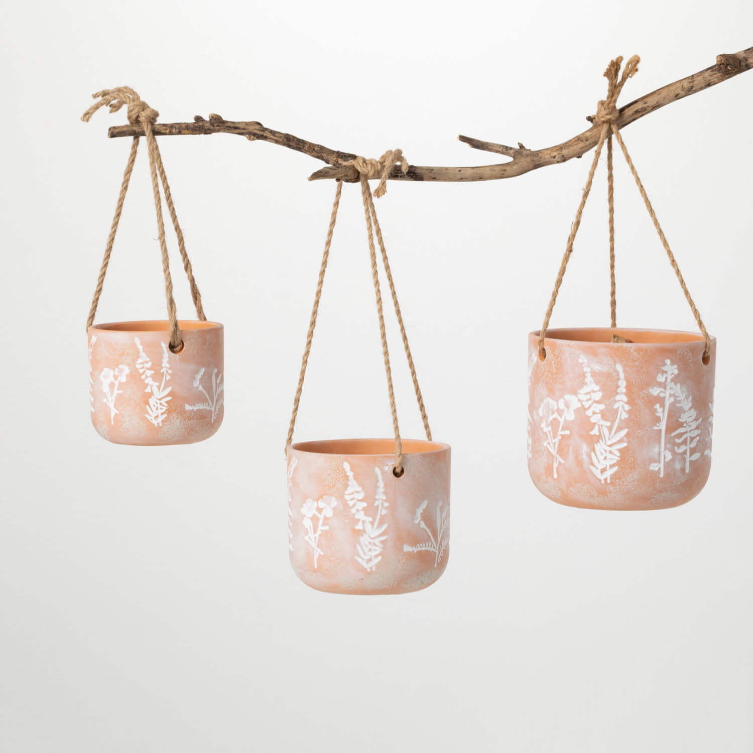 3 sizes of terracotta pots with white herb graphics on them hanging from a  branch on a white background.