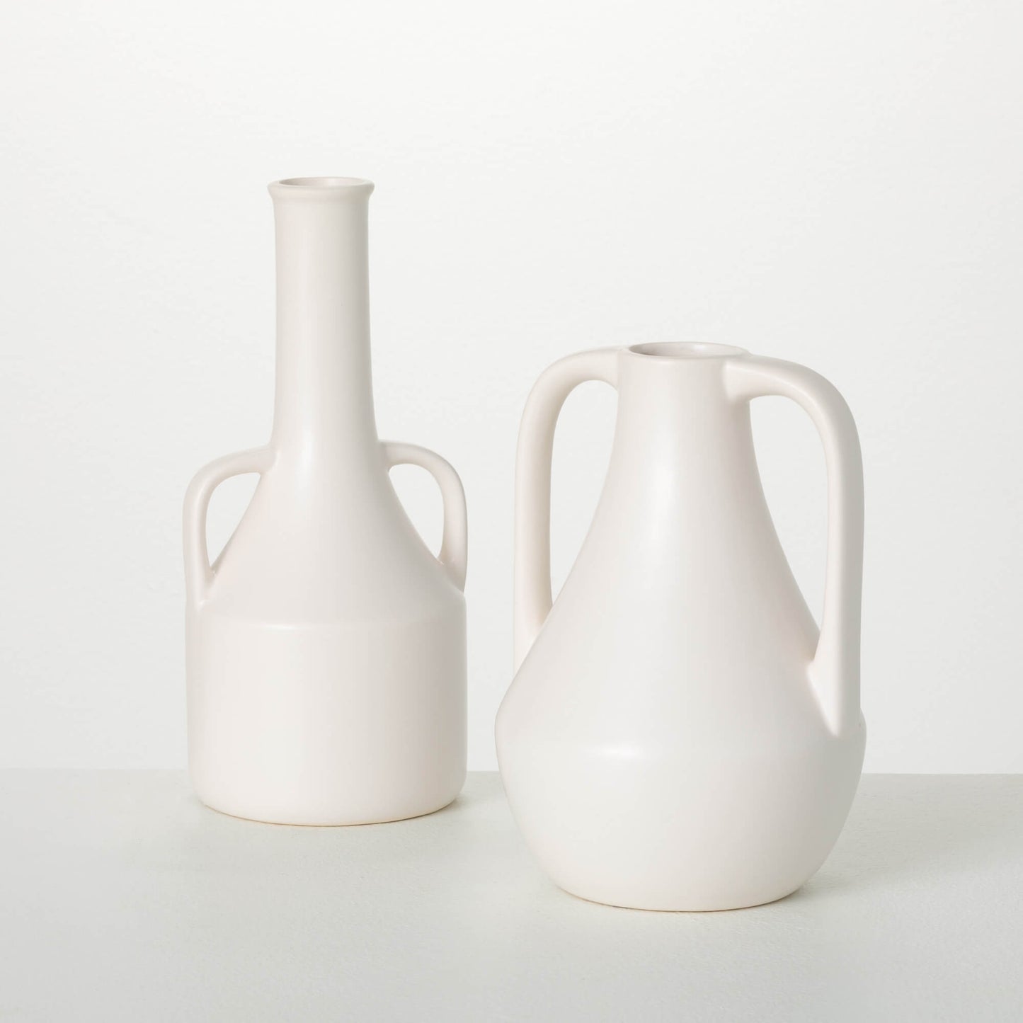 matte creamy white vases with wide bases, narrow necks, and curved side handles.