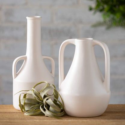 vases set on a wooden table with a sprig of greenery between them.