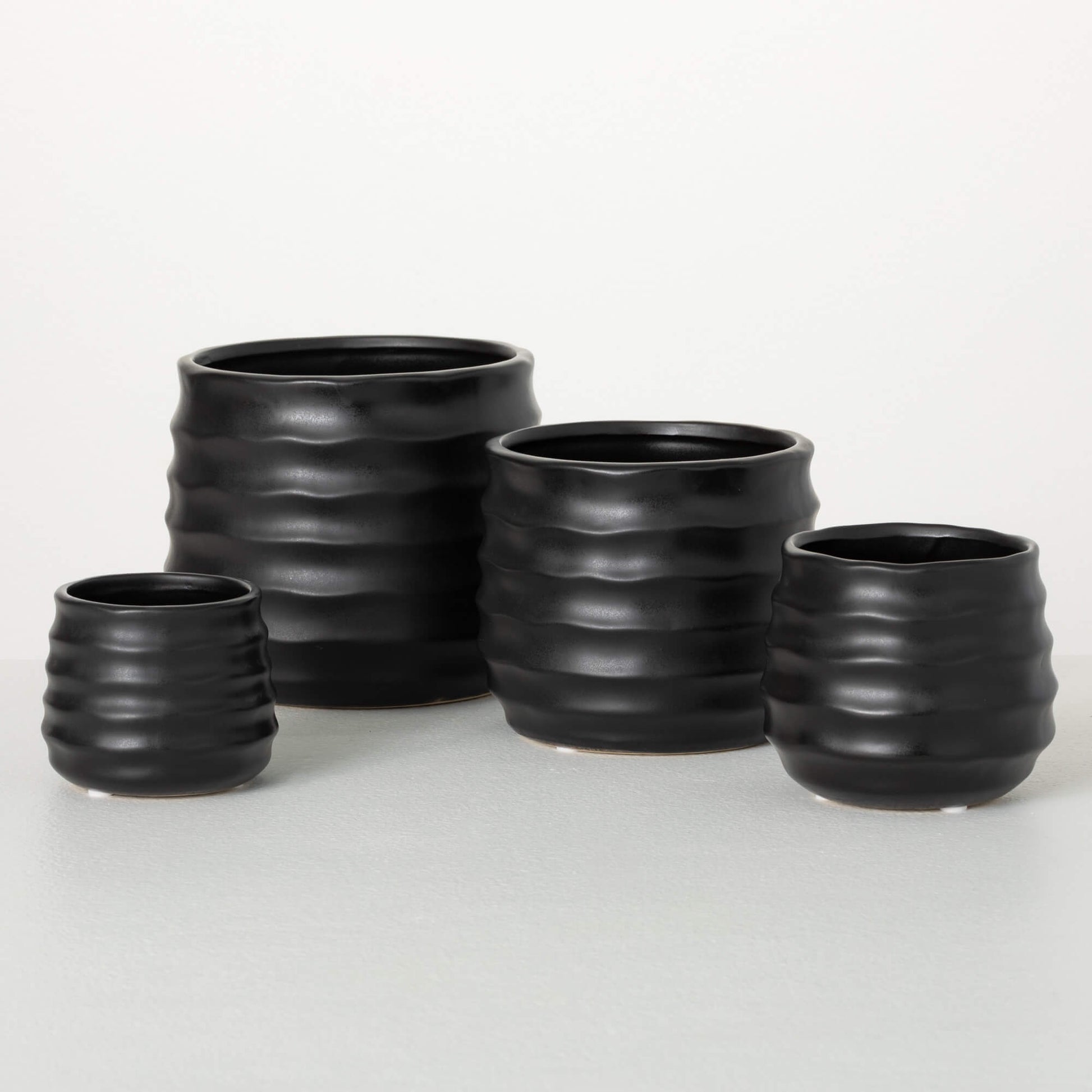 4 sizes of matte black pots woth wavy ribbed lines around the exterior.