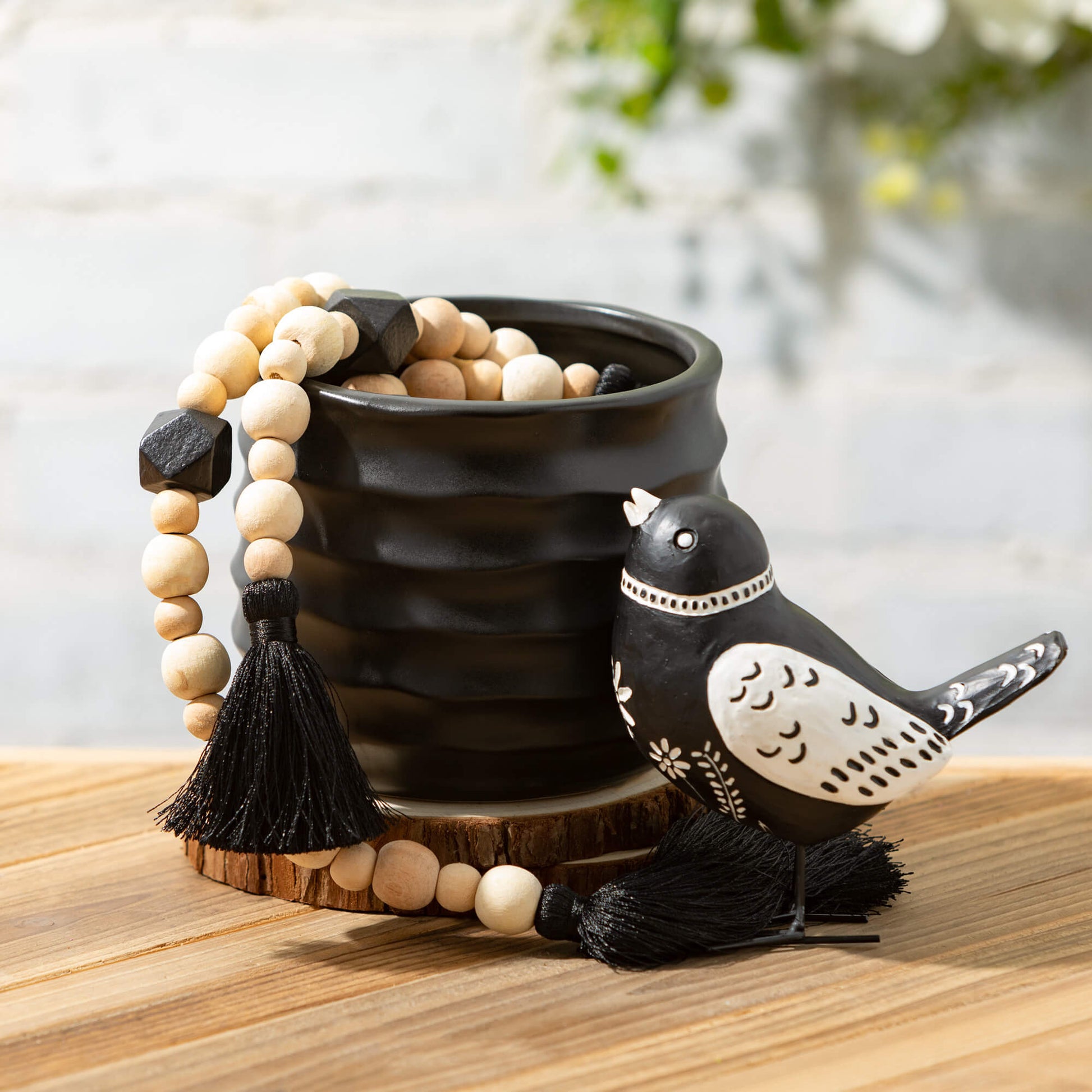 black pot set on piece of wood with a beaded garland draped over it and a wooden bird set next to it.