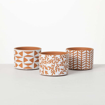 3 terracotta pots with geometric or botanical designs on a white backgroud.
