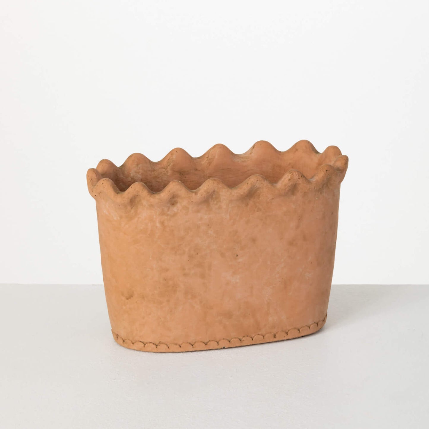 oval terracotta planter with ruffled edge on white background.