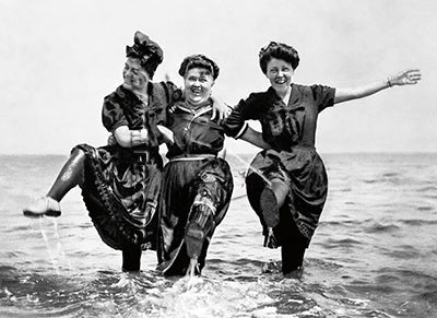 front of card black and white picture of three women playing in the ocean